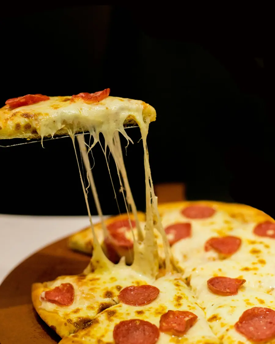 A slice of pepperoni pizza lifted with a long cheese pull